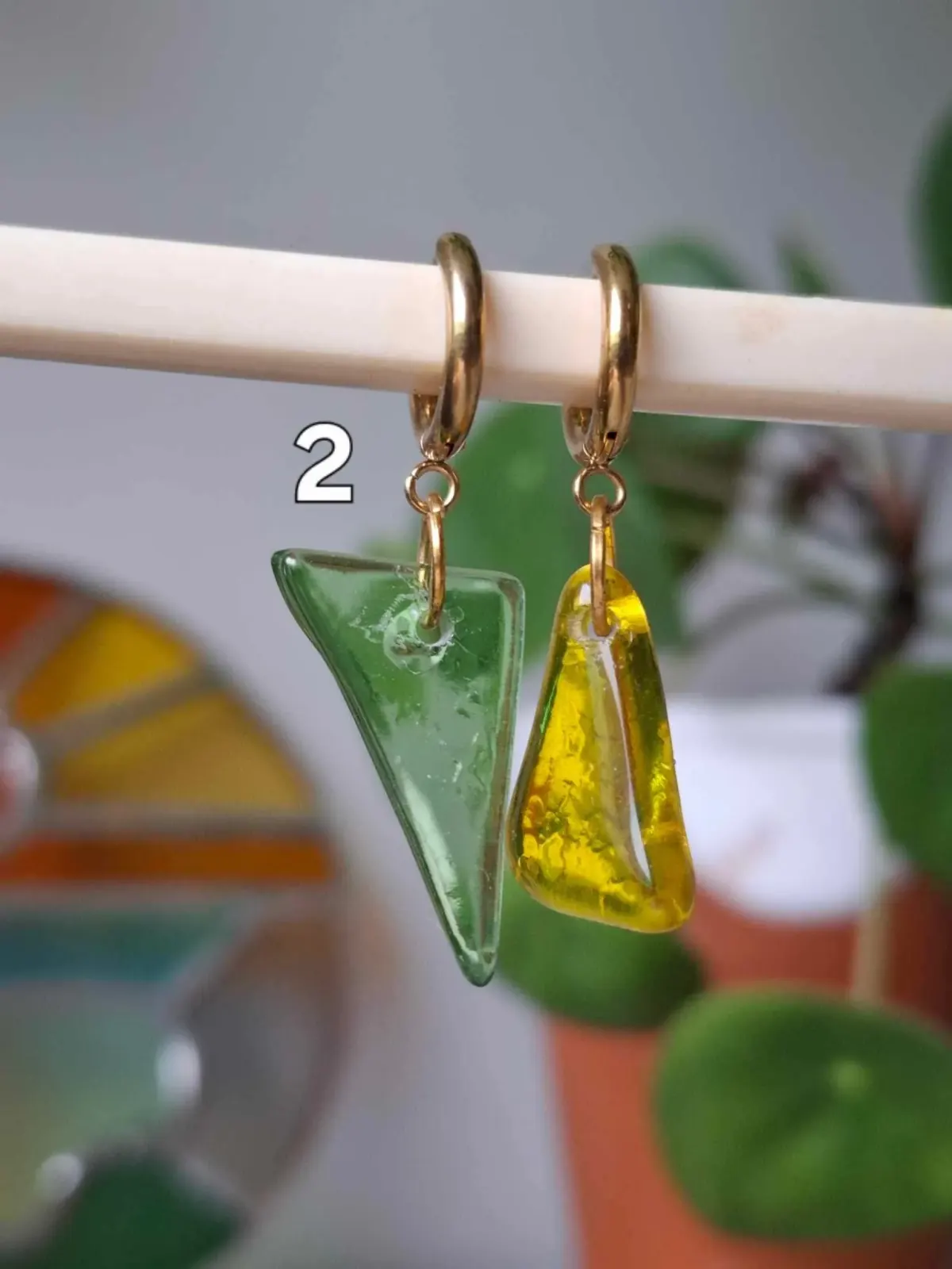 Boucles d'oreilles asymétriques avec un pendant vert et un pendant jaune translucides sur créoles dorées.
