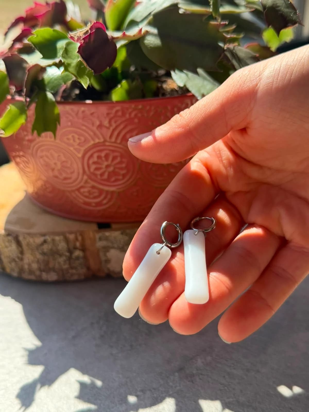 Paire de boucles d'oreilles pendantes en verre blanc tenue dans la main à la lumière du soleil.