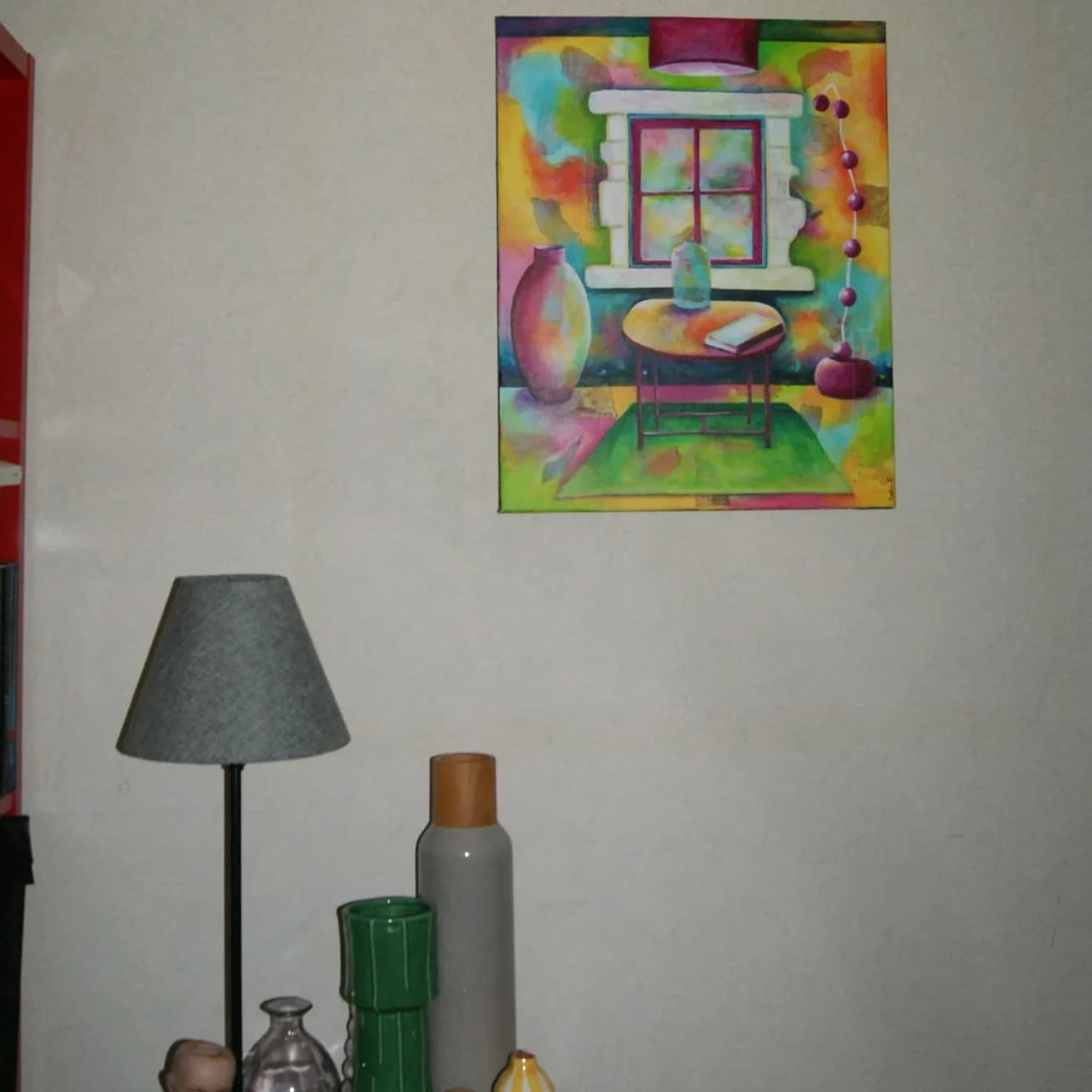 Toile peinte colorée exposée sur un mur au-dessus d'une lampe grise et de vases décoratifs.