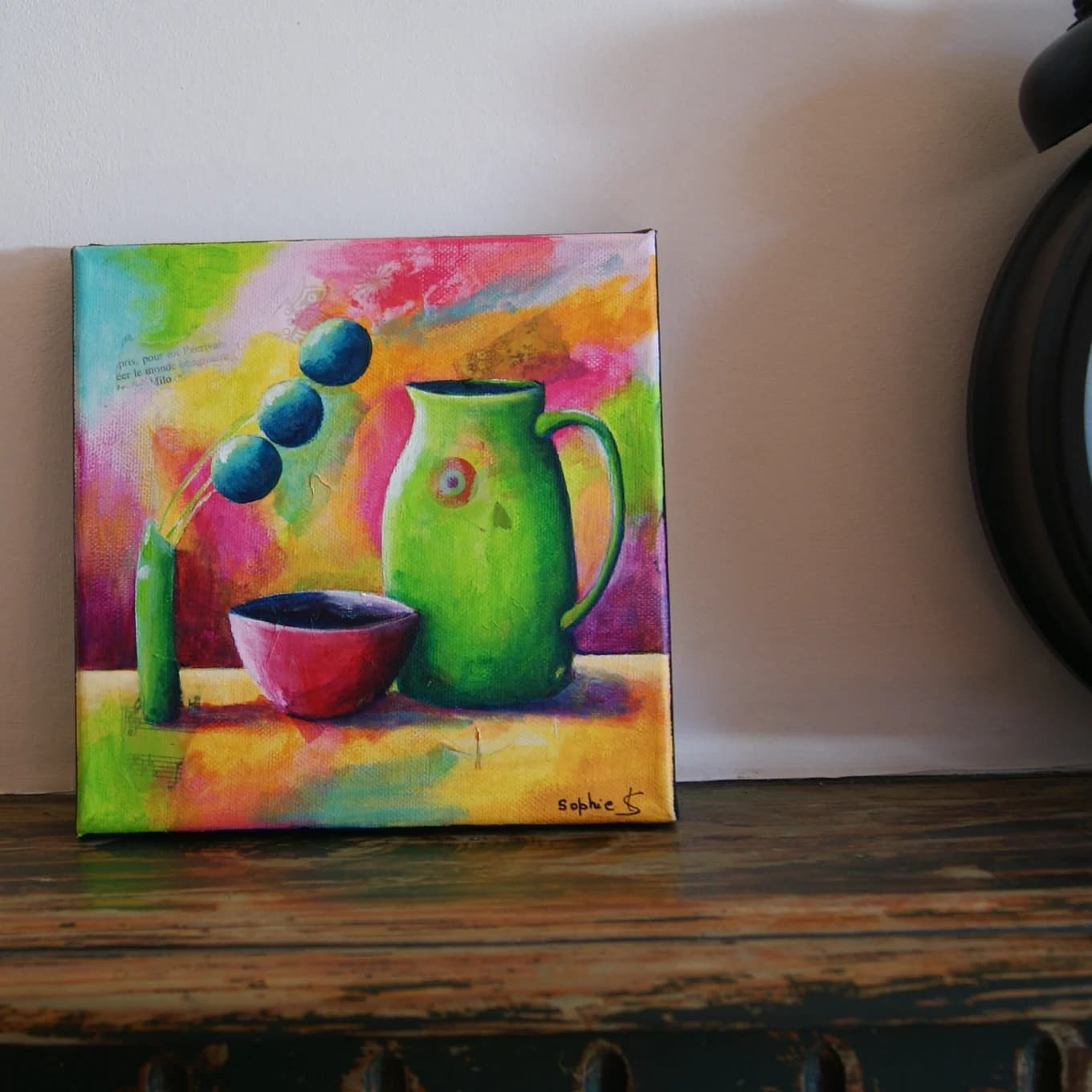 Tableau carré Le pichet vert posé sur un meuble en bois, représentant une nature morte vive et colorée.