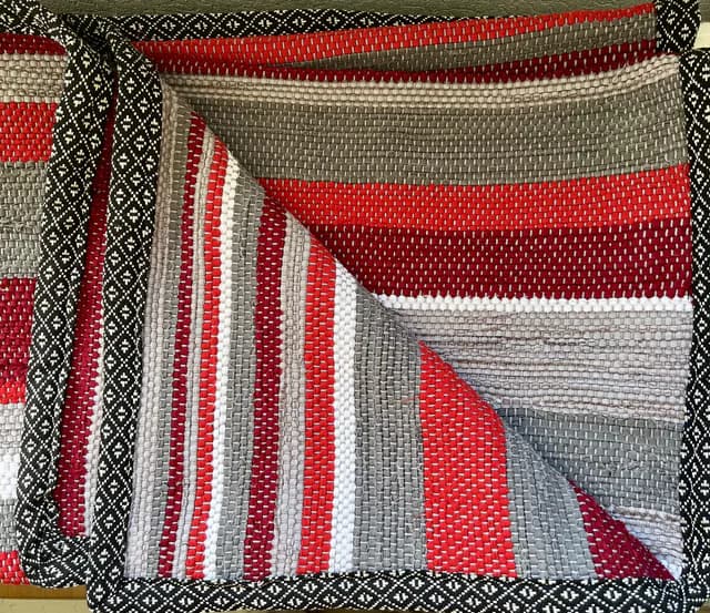 Plaid tissé à rayures rouges, grises et blanches avec bordure géométrique noire et blanche.
