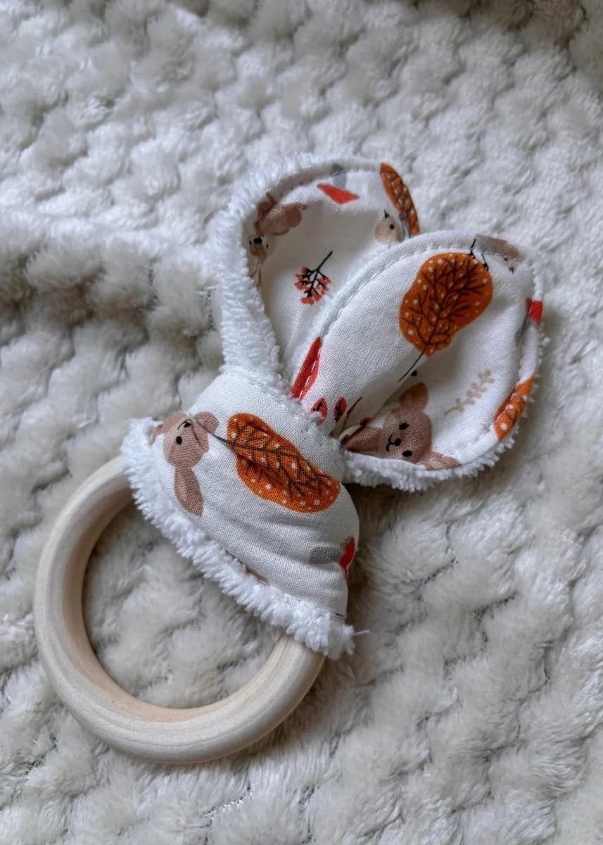 Anneau de dentition en bois avec oreilles de lapin en tissu aux motifs d'arbres d'automne et petits animaux.