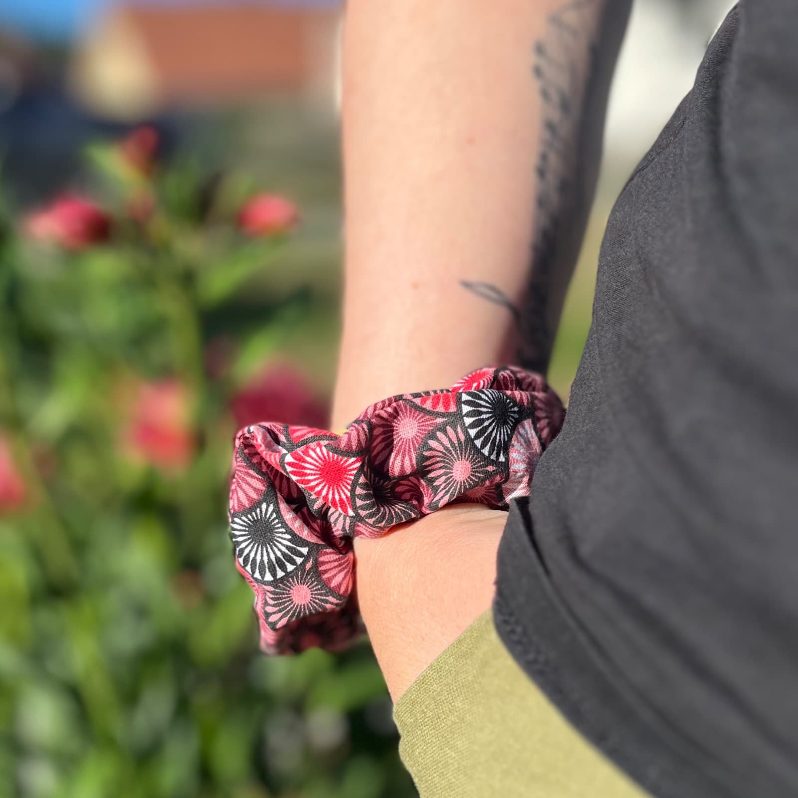 Chouchou en tissu froncé à motifs graphiques roses, rouges et noirs porté au poignet en extérieur.