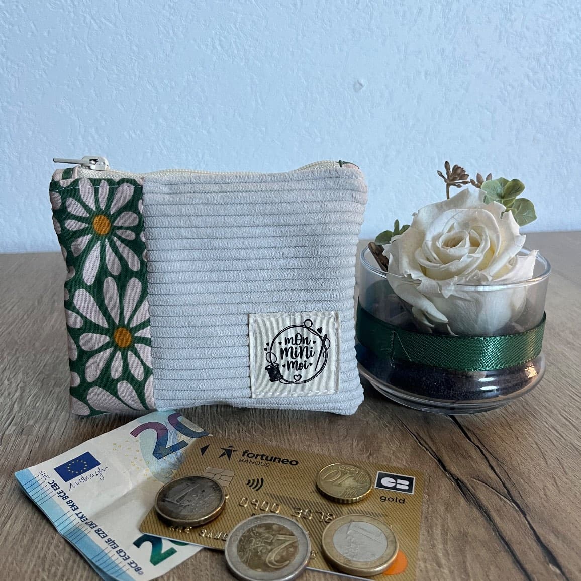 Porte-monnaie en velours côtelé beige et tissu fleuri vert, posé avec monnaie et carte bancaire.
