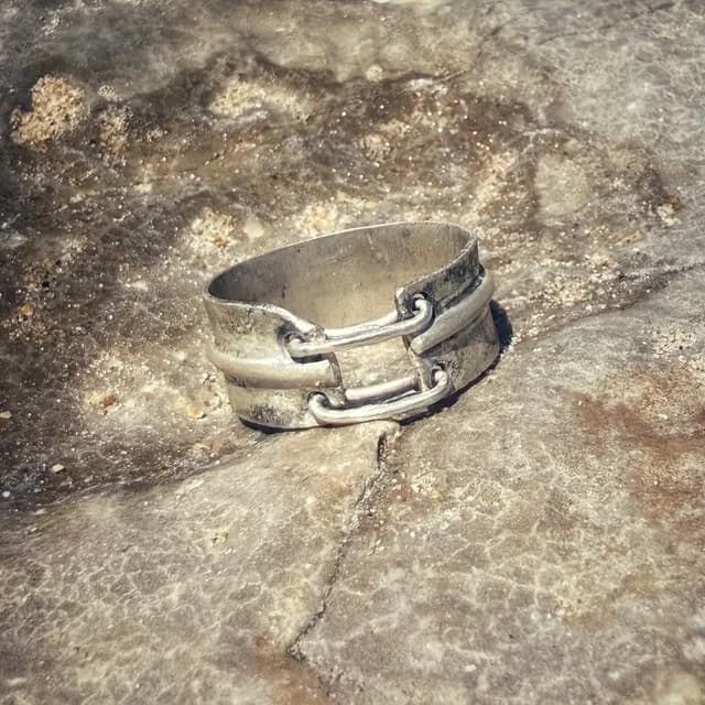 Bague large argentée avec deux attaches mobiles posée sur une roche texturée