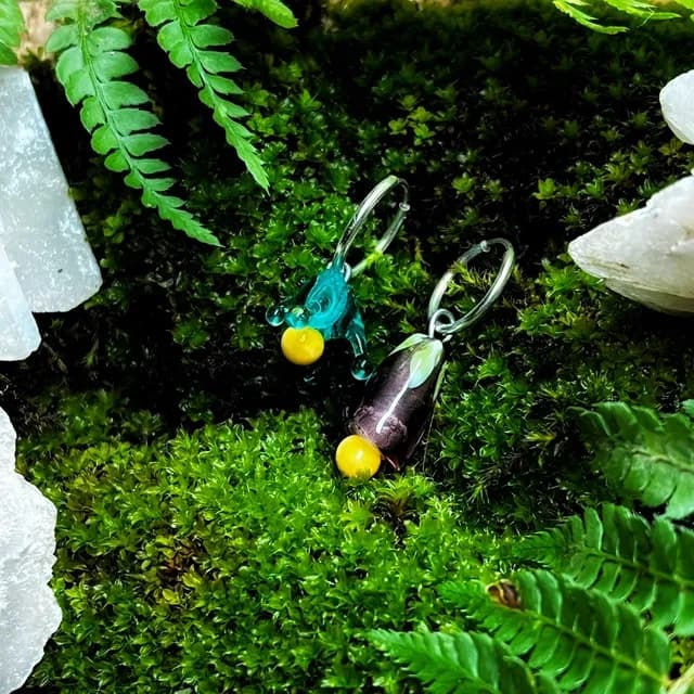 Paire de créoles avec pendentifs en verre asymétriques turquoise et violet sur mousse verte.