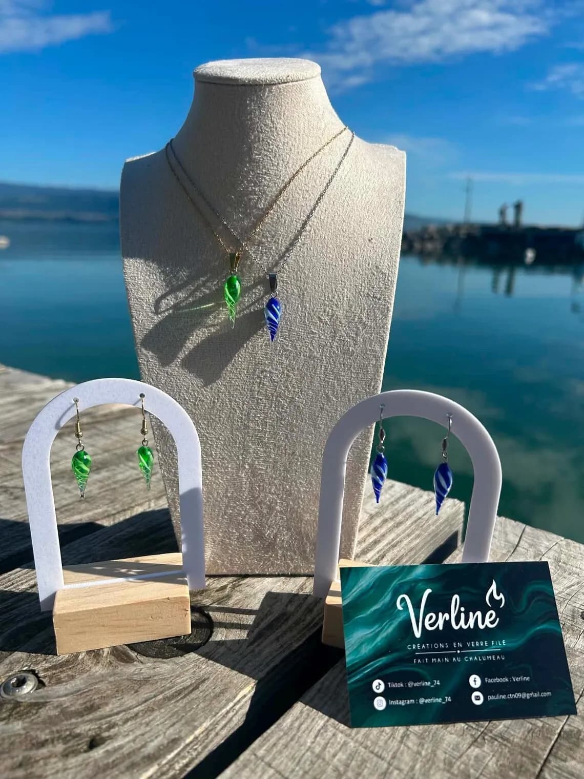 Colliers et boucles d’oreilles torsadées en verre vert et bleu sur présentoirs au bord de l'eau